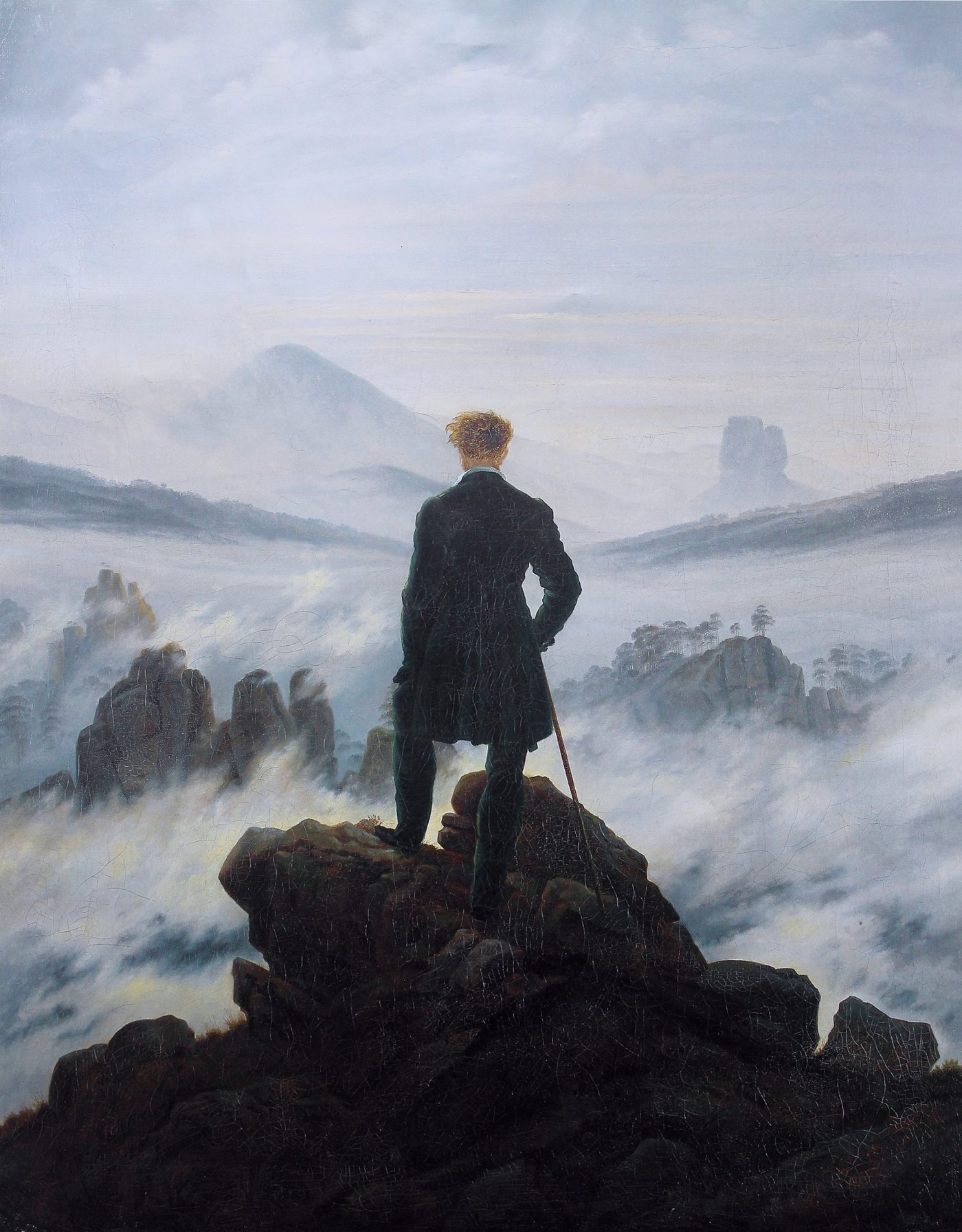 Un voyageur de dos, debout sur un rocher, contemple une mer de nuages